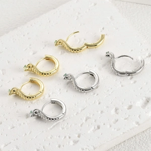 Détail de créoles serpent plaquées or 14k avec yeux en pierres vertes sur support pierre