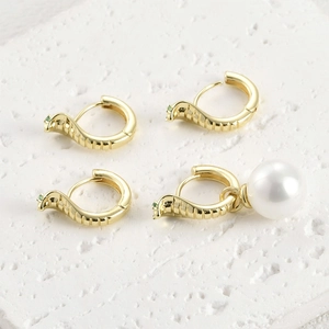 Détail de boucles d'oreilles serpent dorées avec pierres vertes et perle blanche