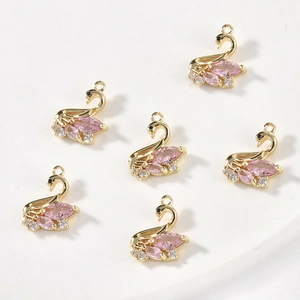 Macro detail of six 14k gold-filled pink swan pendants with sparkling zircon gemstones