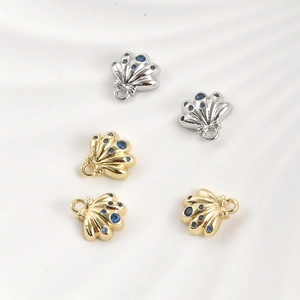 Gold and silver shell charms with blue zircon inlay on white silk fabric background