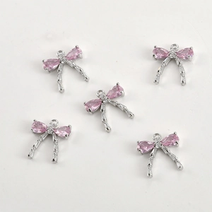 Detailed view of silver bow pendants with pink stones and zircon tassels for DIY jewelry