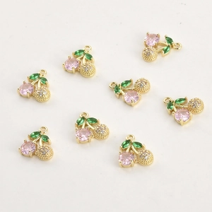Flat lay of 14k gold plated cherry pendants with pink zircon and green leaves