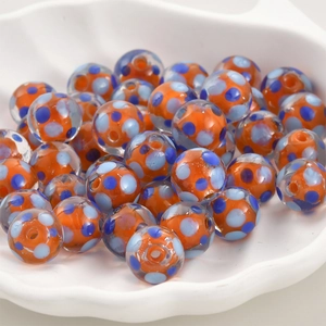 Nahaufnahme von orangen Lampwork-Glasperlen mit blauen Punkten für DIY-Schmuckdesign