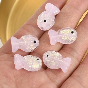 Macro shot of 5 pink translucent fish-shaped resin beads with sparkling gold foil