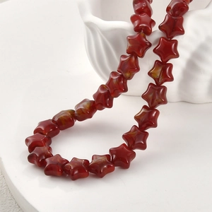 Nahaufnahme handgefertigter roter Glasperlen in Sternform für DIY-Schmuck auf Keramikschale