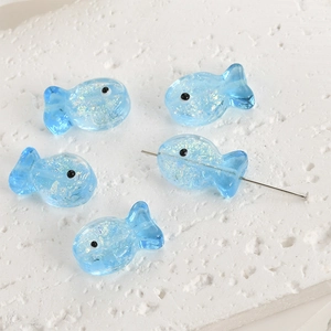 Macro shot of light blue fish-shaped glass beads with sparkling foil for DIY jewelry