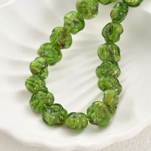Macro detail of translucent green glass rose beads in a white shell dish for DIY jewelry