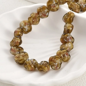 Macro view of amber handmade glass rose beads with carved petal details on white shell tray