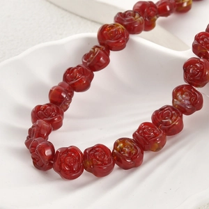Macro view of detailed red glass rose beads with textured petals on a shell display