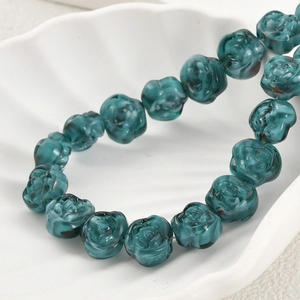 Macro shot of dark turquoise glass rose beads in a white shell dish for jewelry making