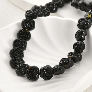 Detailed view of black glass rose beads with intricate petal textures in a white shell dish