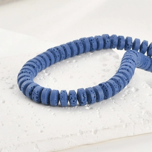 Makroaufnahme von 4x8mm blauen Lavastein-Scheibenperlen auf weißem strukturiertem Stein
