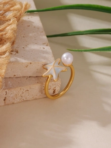 Dettaglio dell'anello a stella marina dorata con perla su pietra e ombre di foglie