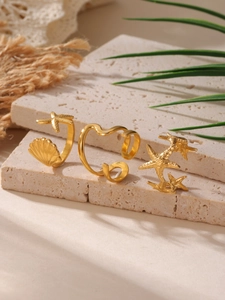 Λεπτομέρεια τριών επίχρυσων δαχτυλιδιών 18K με αστερίες και κοχύλια σε μπεζ πέτρα