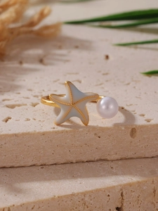 Dettaglio anello aperto con stella marina dorata e perla su base di marmo beige