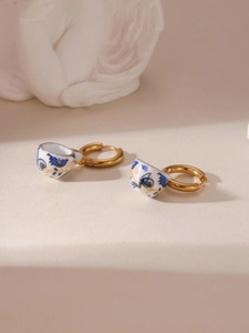 Detailed macro view of 18K gold-plated hoops with miniature blue floral porcelain teacups