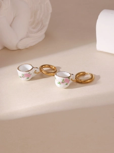 Detailed macro of gold-plated hoop earrings with floral ceramic teacup charms on stone