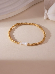 Detailed shot of gold beaded bracelet featuring a white bone charm on cream background