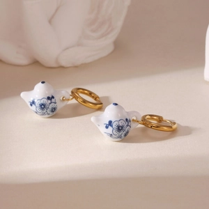 Blue and white porcelain teapot earrings with 18K gold plated hoops on a minimalist surface
