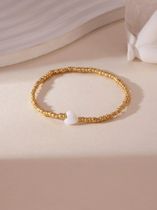 Detailed view of an 18K gold-plated beaded bracelet with a white shell heart charm