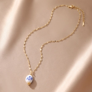 Detail of blue and white floral porcelain bead pendant with gold chain on silk fabric