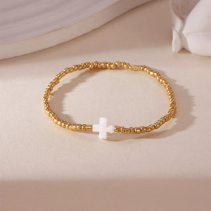 18K gold plated bead bracelet with white cross charm on minimalist cream background