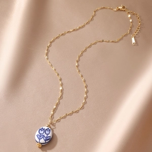 Detail of 18K gold-plated necklace with blue tulip ceramic pendant on champagne satin