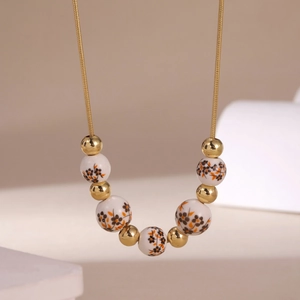 Close-up of a gold snake chain necklace with floral ceramic beads and 18K gold-plated spacers
