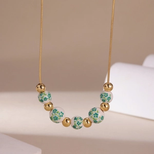 Detail of 18K gold chain necklace with floral ceramic beads and shiny golden spheres