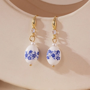 Macro shot of blue and white floral porcelain earrings with gold hooks and pearl accents