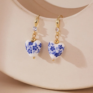 Detailed close-up of heart-shaped blue and white porcelain earrings with gold hooks