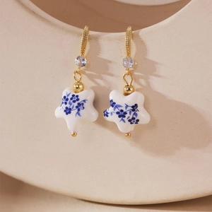 Detail of star-shaped blue and white porcelain earrings with gold hooks and tiny crystals