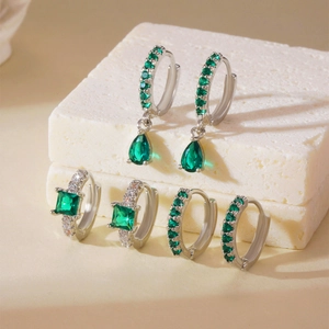 Three pairs of silver earrings with green square zircon stones on marble display