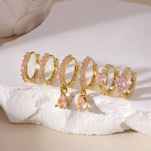 Close-up of gold plated huggie earrings set with pink cubic zirconia on white stone