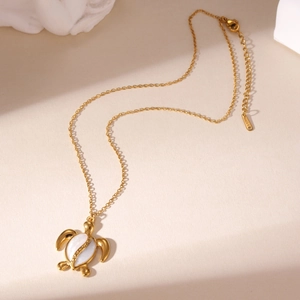 Gouden roestvrijstalen ketting met schildpad hanger en schelpinleg op beige achtergrond