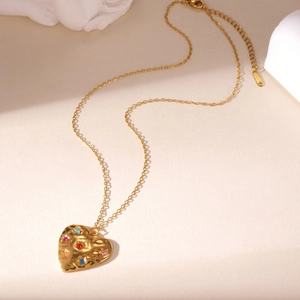 Detail of gold-plated stainless steel heart pendant with colorful stones and hammered finish