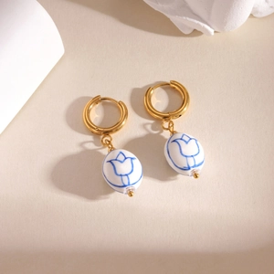 Vintage blue tulip porcelain earrings with golden metal rings on a warm neutral background