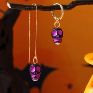 Vista macro di orecchini a teschio asimmetrici placcati oro con dettagli viola per Halloween