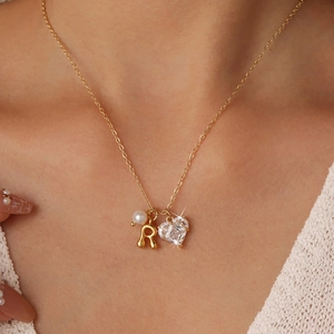 Women's gold heart necklace with zircon, pearl, and letter R pendant on a model