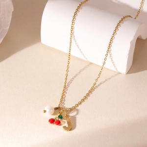 Gold cherry fruit necklace with letter J pendant and pearl on white geometric stand