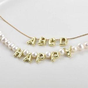 Detail of 14k gold-plated 3D letter charms and pearls on necklace for DIY jewelry making