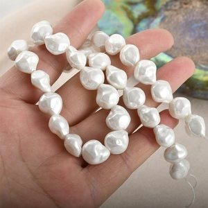 Strand of irregular white Baroque glass pearls for jewelry making held in hand over shell
