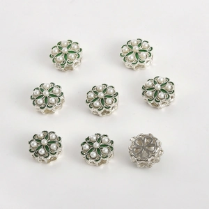 Dettaglio di ciondoli a forma di fiore con smalto verde e perle d'imitazione bianche