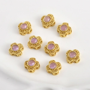 Dettaglio di perline a quadrifoglio dorate con design filigranato e perla rosa