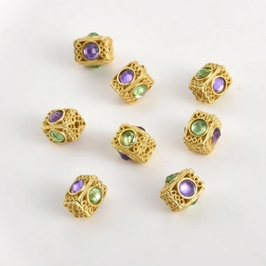 Dettaglio macro di perline distanziatrici a fiori dorati con cristalli viola e verdi per gioielli