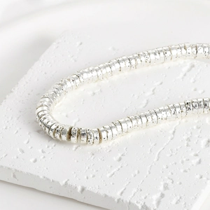 Detailed close-up of 4mm silver lava wheel spacer beads on white stone background