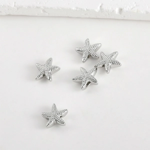 Close-up of five silver starfish charms with beads and textured details on white surface