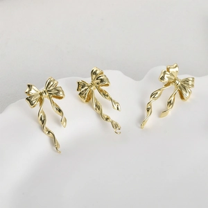 Three gold-plated bow ribbon pendants for DIY earrings on a white ceramic plate