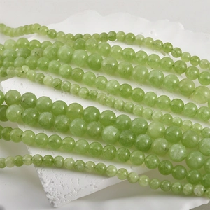 Multiple sizes of natural green jade round beads for DIY jewelry making on white stone