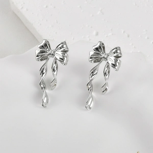 Detail of elegant silver bow earrings with polished metal finish on a white tray